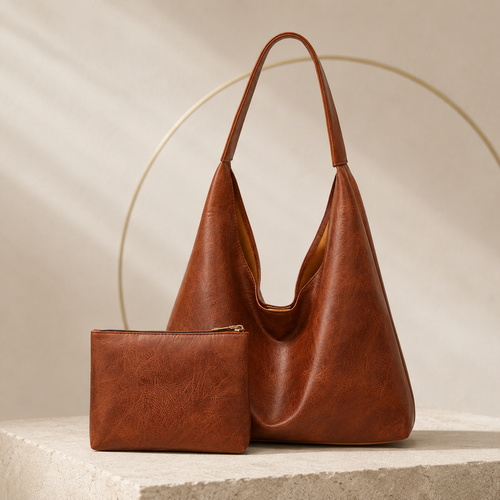 A brown leather hobo shoulder bag with a matching zippered pouch, displayed on a light stone pedestal against a beige background with soft shadows and a thin circular wire decoration.