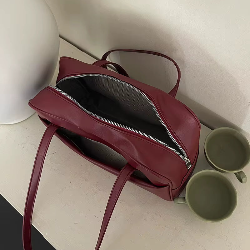 Red handbag with a silver zipper on a light surface next to two green mugs.