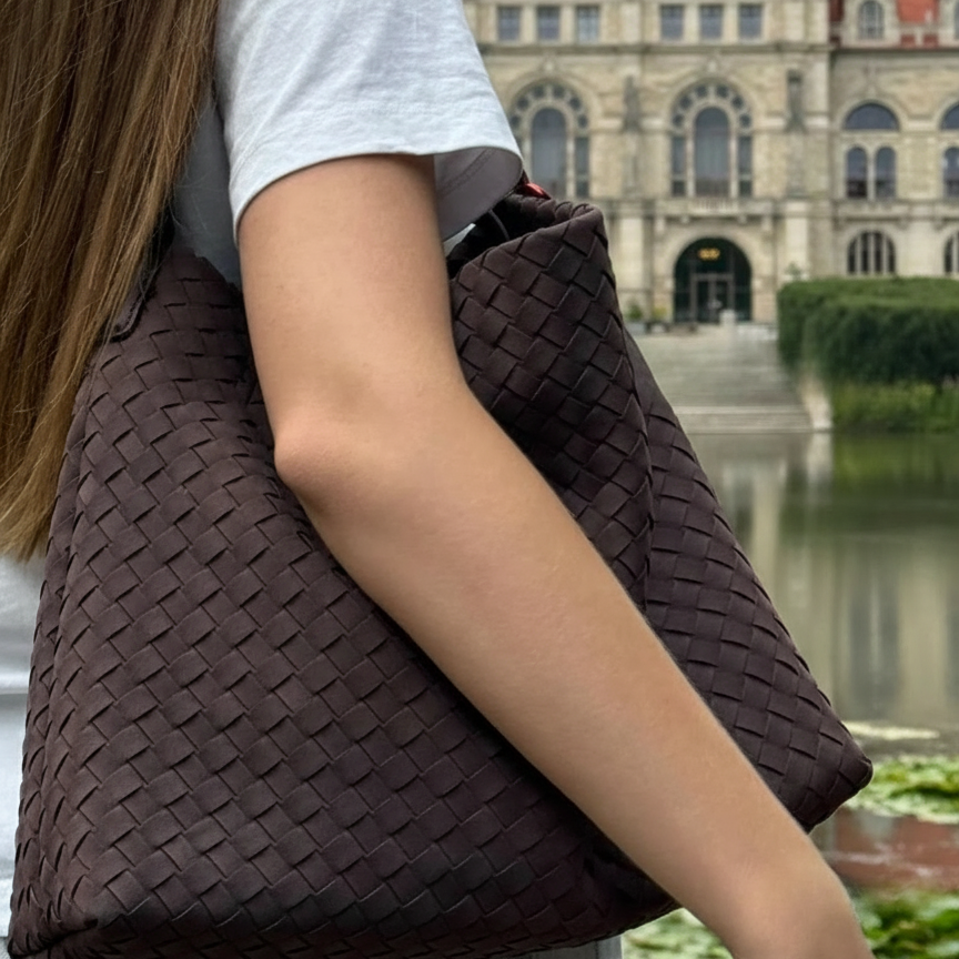 Person holding a woven brown bag with a blurred background of a building and water.