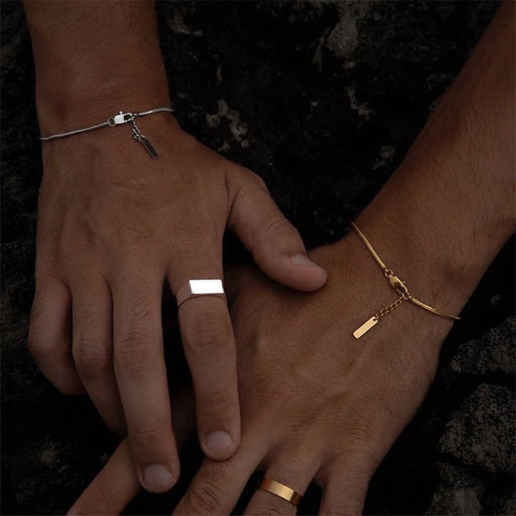 Two hands resting on a dark textured surface, showcasing minimalist gold and silver rings and bracelets