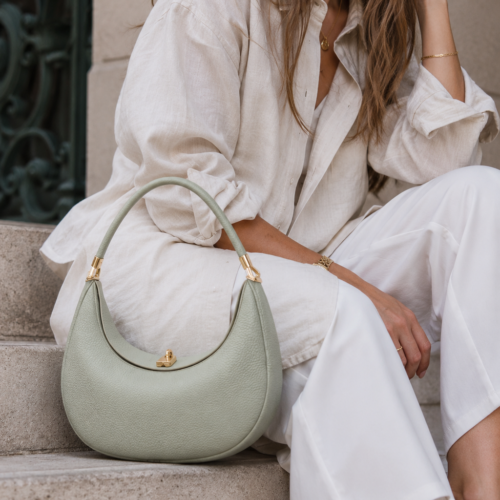 Person holding a light green handbag with gold accents, wearing a white outfit.